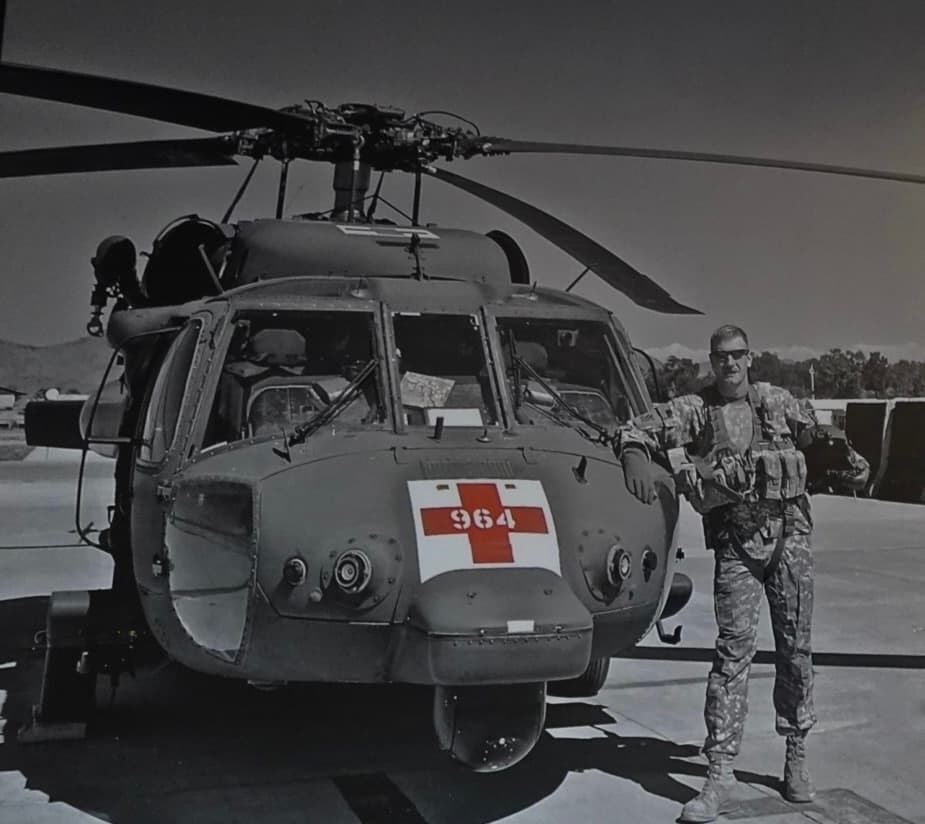 Soldier in camouflage stands beside a military medical helicopter featuring a prominent red cross.